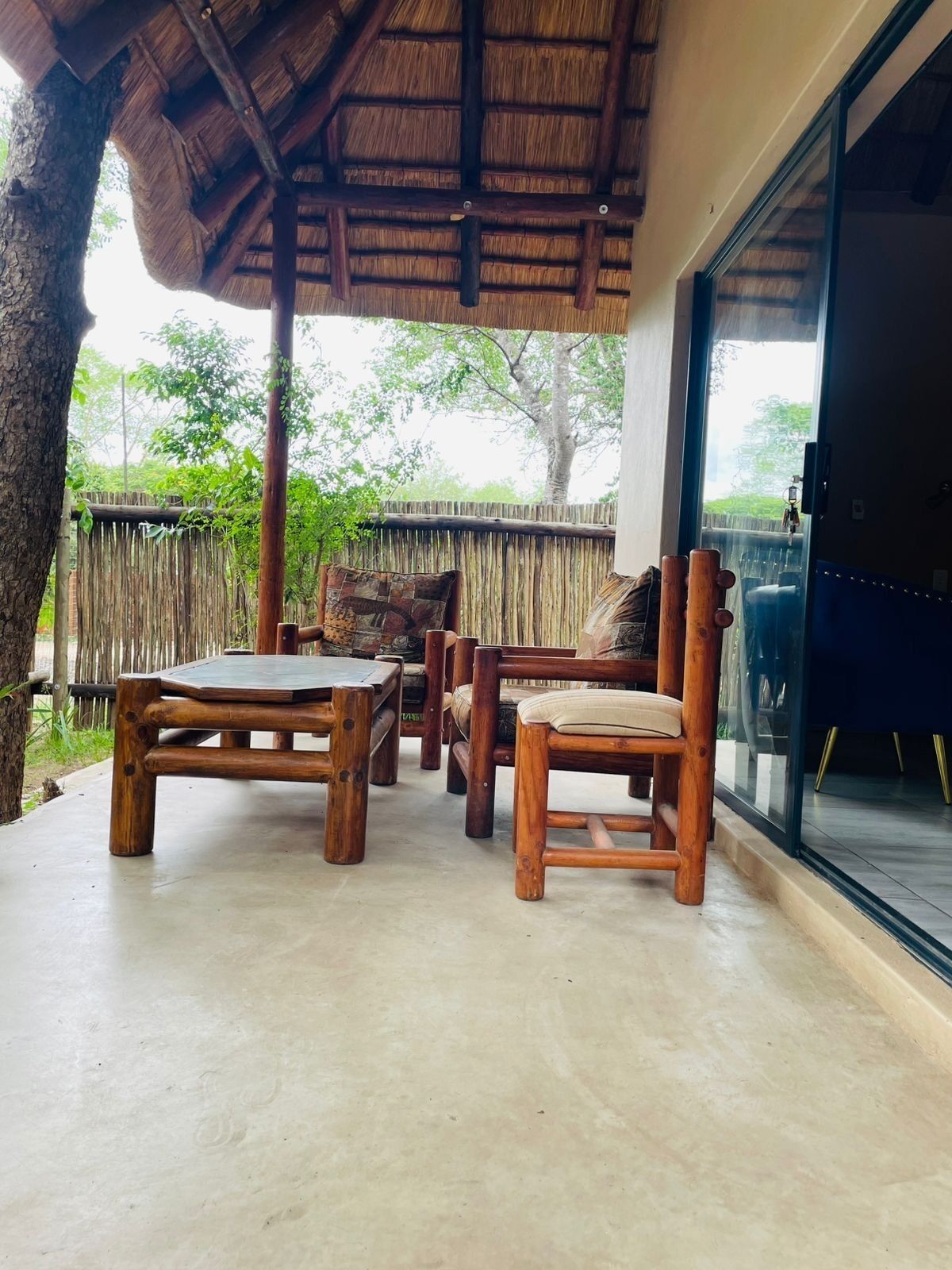 A wooden outdoor seating area with a thatched roof, a cushioned chair, and a table.