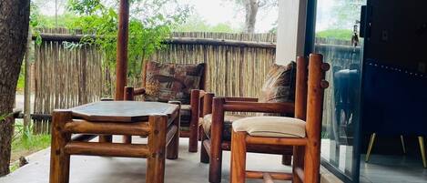 A wooden outdoor seating area with a thatched roof, a cushioned chair, and a table.