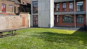 Une cour avec une structure en béton, un bâtiment en briques et une table entourée de chaises.