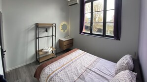 Une chambre à coucher comprenant un lit, une table de chevet, un miroir, une armoire et une fenêtre avec des rideaux.