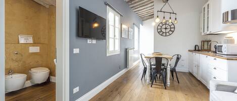 A modern kitchen with wooden flooring, white cabinets, and a dining area with a table and chairs.