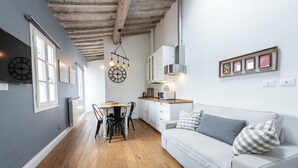 A modern kitchen with wooden flooring, a dining area with a table and chairs, and a light grey sofa with pillows. - Central Nest by MMega (Florence)