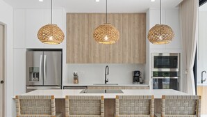 A modern kitchen with a central island, stainless steel appliances, and woven pendant lights. - Luxury Stay with Private Pool & Family Amenities in a New Resort Community (Hacienda Pinilla)