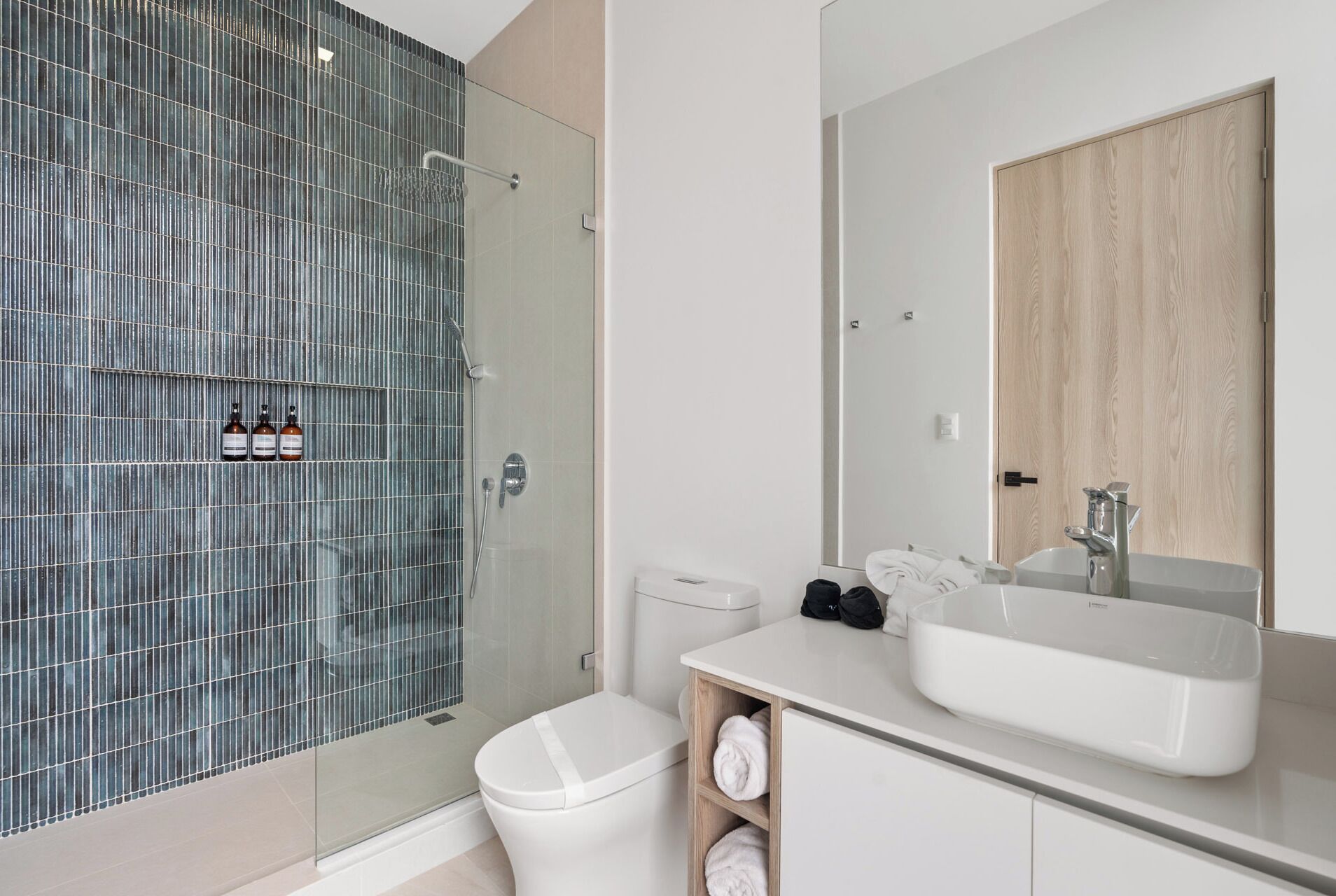 Une salle de bain moderne avec une douche à parois de verre, des toilettes blanches, un lavabo avec un miroir et un meuble en bois.