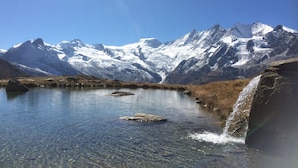 Ein klarer Bergsee mit steinigen Ufern und schneebedeckten Berggipfeln im Hintergrund.