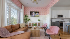 Un salon avec un canapé marron, une table basse en bois et un téléviseur fixé au mur. Il y a également un coin cuisine avec des meubles blancs et des appareils électroménagers en acier inoxydable.