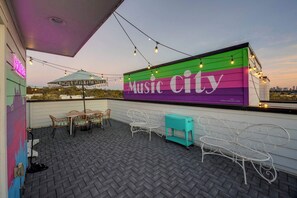 An outdoor patio with a mural reading "Music City," outdoor seating, and string lights. - The Pink Stetson: Rooftop Views, Party Hats, Games (Nashville)