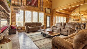 A log cabin interior with a living room, sofas, a fireplace, and a dining area.