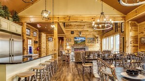 A rustic wooden interior with a bar area, seating, and a fireplace.