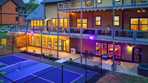 A two-story building with a balcony, outdoor seating, and a tennis court.