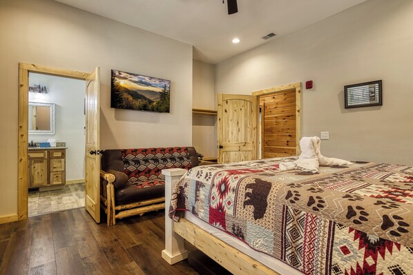 A bedroom with a wooden bed, a patterned sofa, a wooden wardrobe, and a painting on the wall.