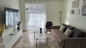 Una sala de estar moderna con un sofá, una mesa de centro y un televisor. Hay una planta en maceta y una lámpara.