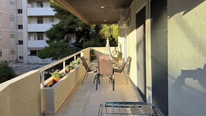 Un balcón con una mesa y sillas, plantas en macetas y vistas a edificios cercanos.