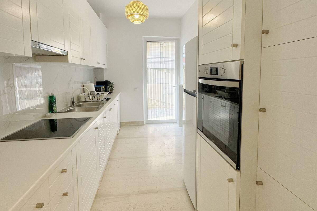 A modern kitchen with white cabinetry, a built-in oven, and a pendant light.