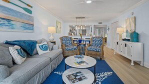 Una sala de estar con un sofá gris, sillas con estampado azul y blanco, una mesa de comedor y una consola blanca.