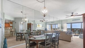 A dining area with a glass table, chairs, and hanging lights. There is a ceiling fan and a sign reading 'BEACH HOUSE'. - Palms 915- Premier beachfront condo, 3 bedrooms, sleeps 8, 9th floor (Orange Beach)