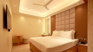 A modern hotel room with a large bed, a ceiling fan, a bedside table with a lamp, and a small round table. - Park Residency Kanchipuram (Kanchipuram)