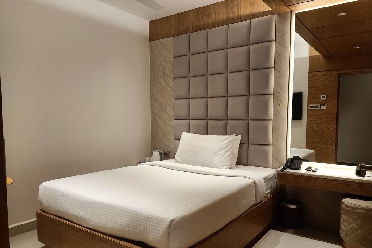Ein modernes Schlafzimmer mit einem großen Bett, einem Holzkopfteil, einem Nachttisch mit Telefon und einem Spiegel.