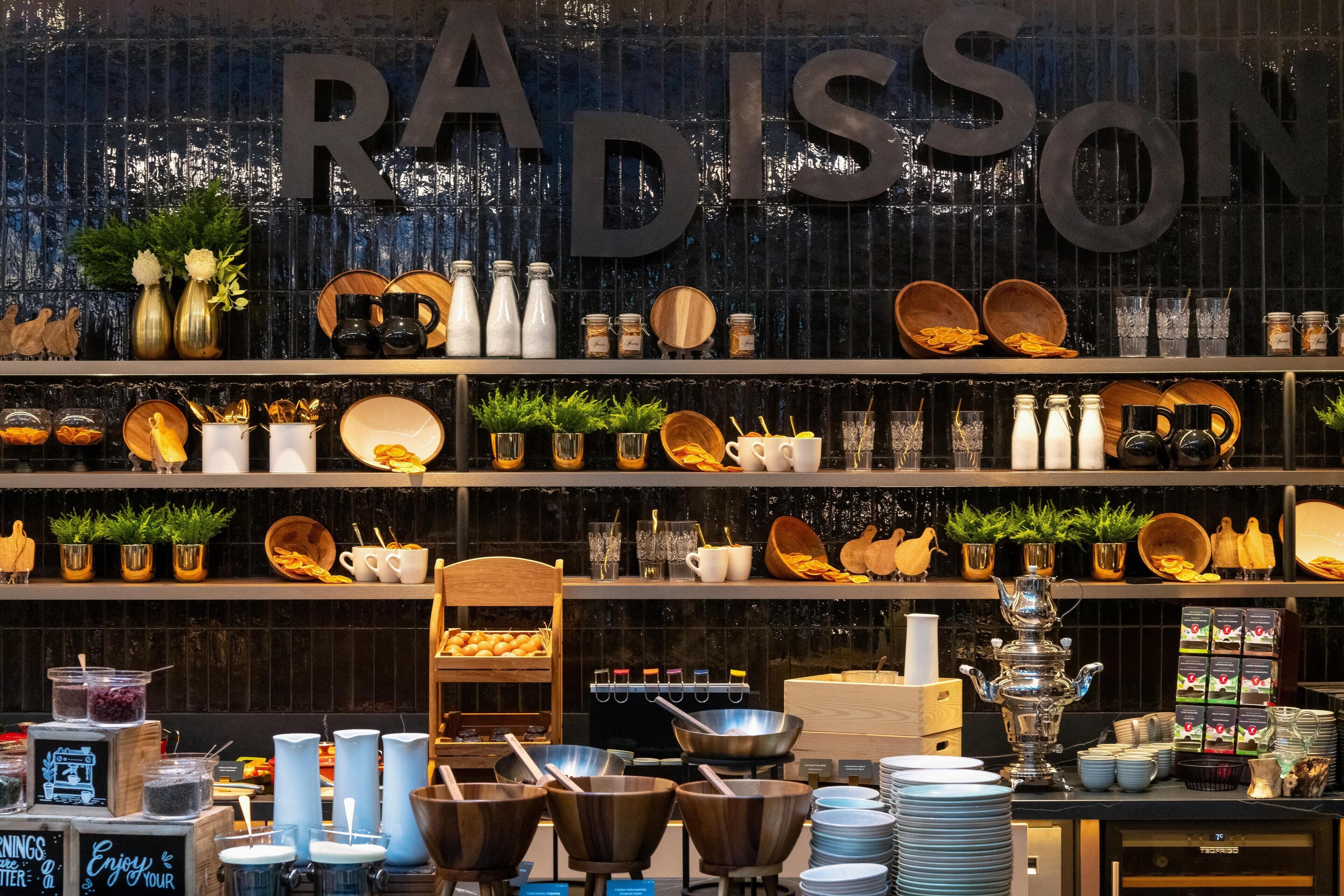 Un coin cuisine avec des étagères où sont exposés divers ustensiles de cuisine, un panneau noir et un grand panneau métallique sur lequel on peut lire « RADISSON ».