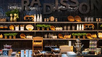 Un coin cuisine avec des étagères où sont exposés divers ustensiles de cuisine, un panneau noir et un grand panneau métallique sur lequel on peut lire « RADISSON ».