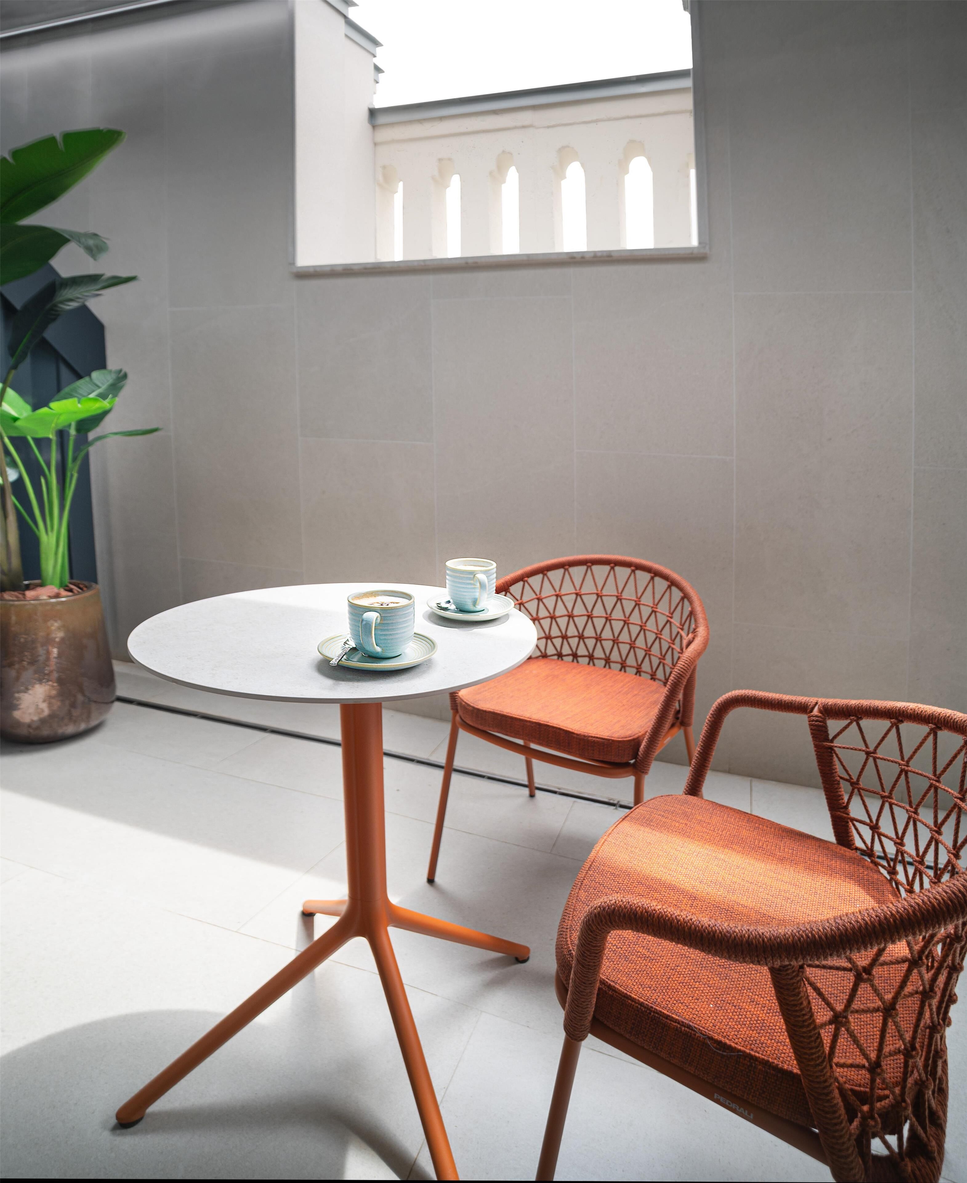 A round table with two chairs, a potted plant, and a window with arches.