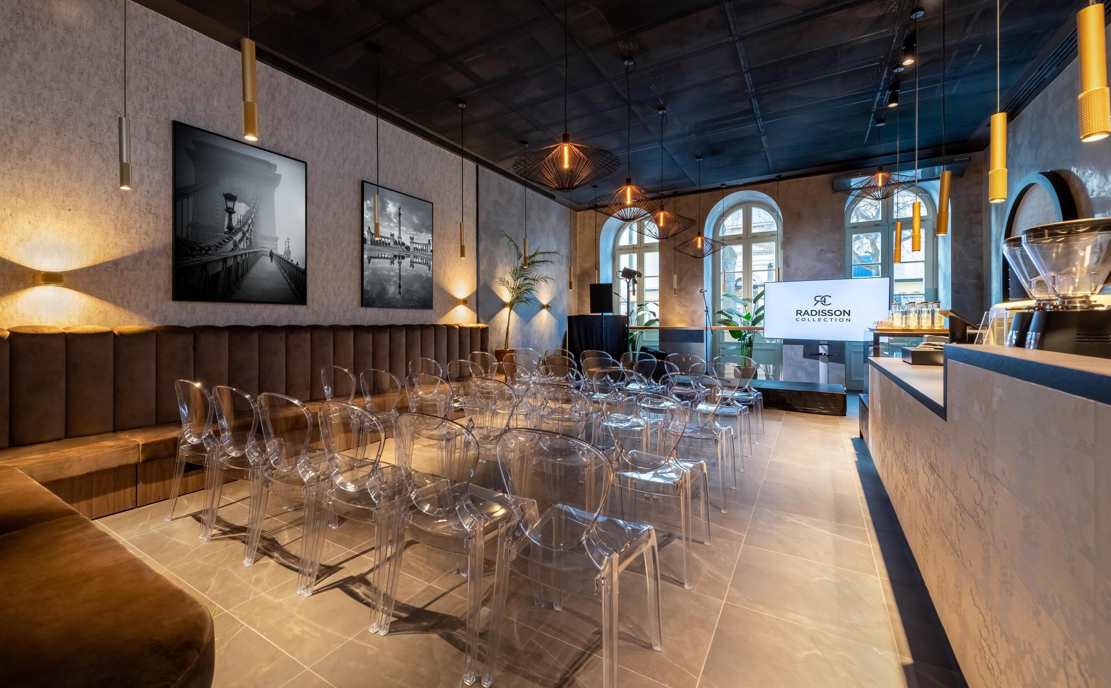 Un comedor moderno con sillas traslúcidas, una mesa larga y una zona de bar con una pantalla de televisión que muestra 'RADISSON COLLECTION'.