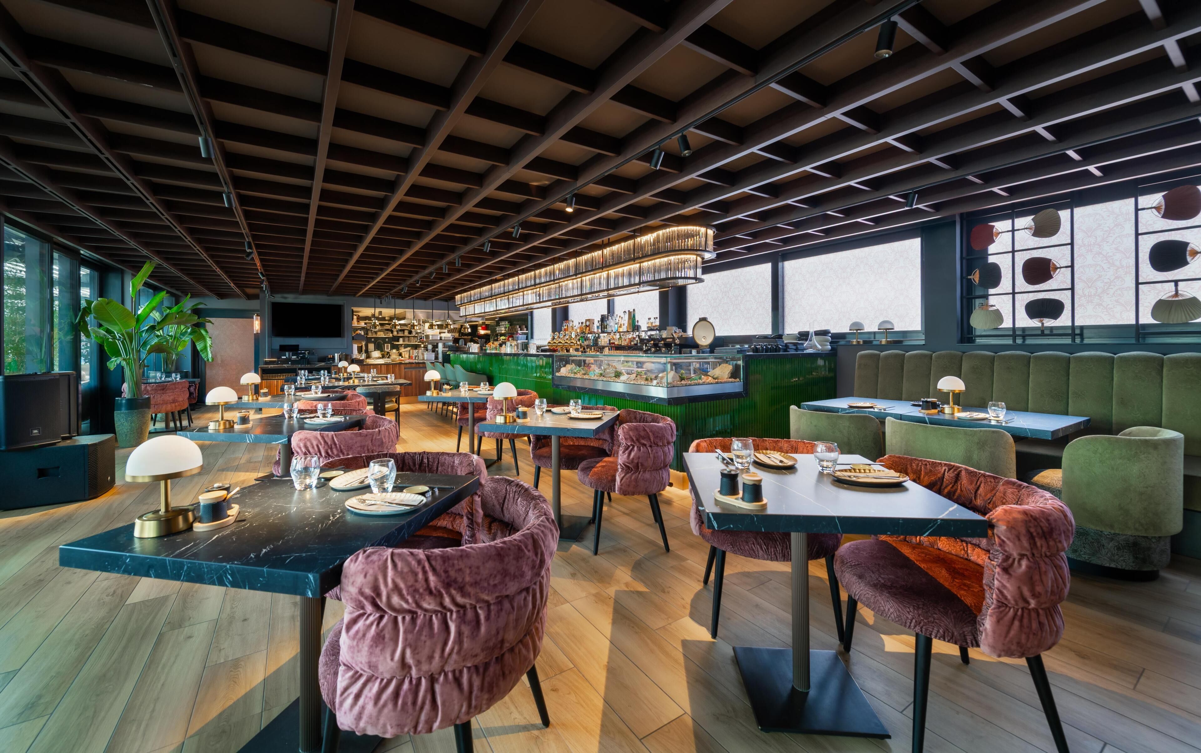 A modern restaurant interior with high ceilings, exposed beams, and a bar area with a variety of bottles.