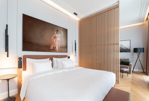 Una camera d'albergo moderna con un grande letto, una testiera in legno, un quadro di grandi dimensioni, un divisorio in legno, un comodino, una lampada da terra, un divano e un tavolino da caffè.
