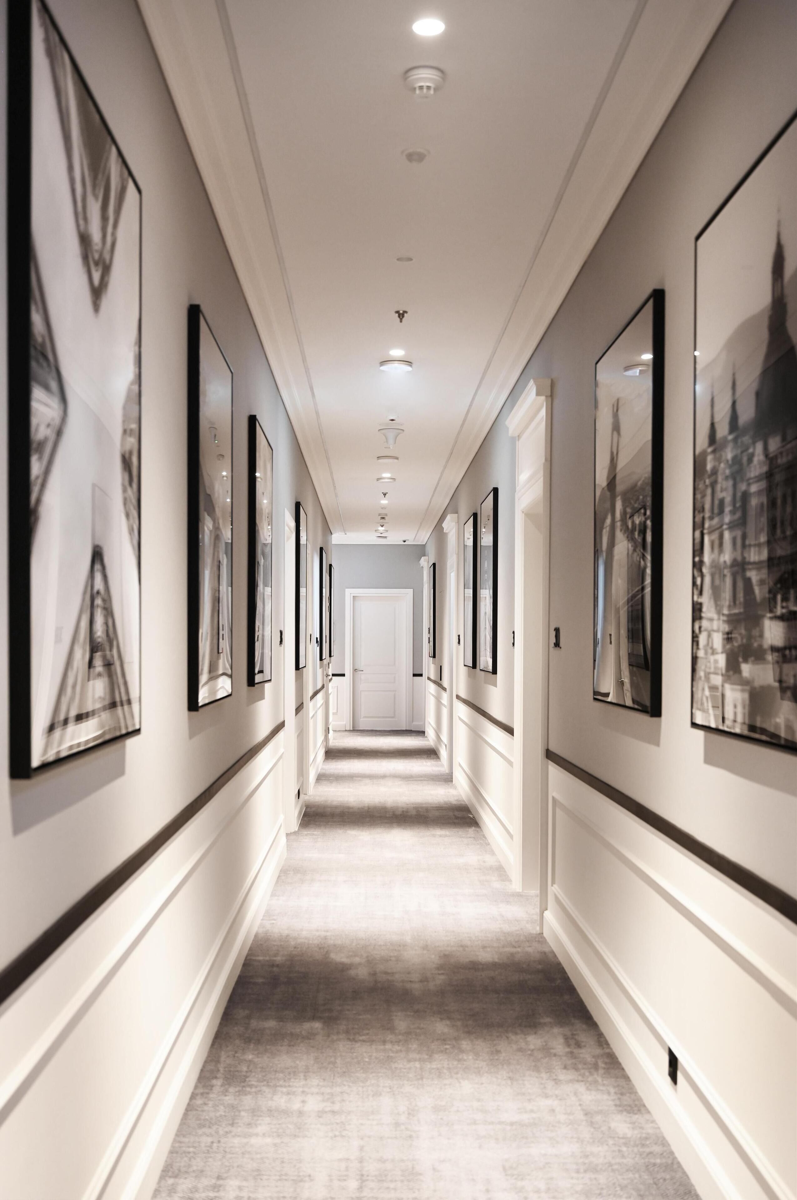 A hallway with framed artwork on the walls, a carpeted floor, and a door at the end.