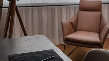 A room with a table, a chair, a lamp, and sheer curtains.