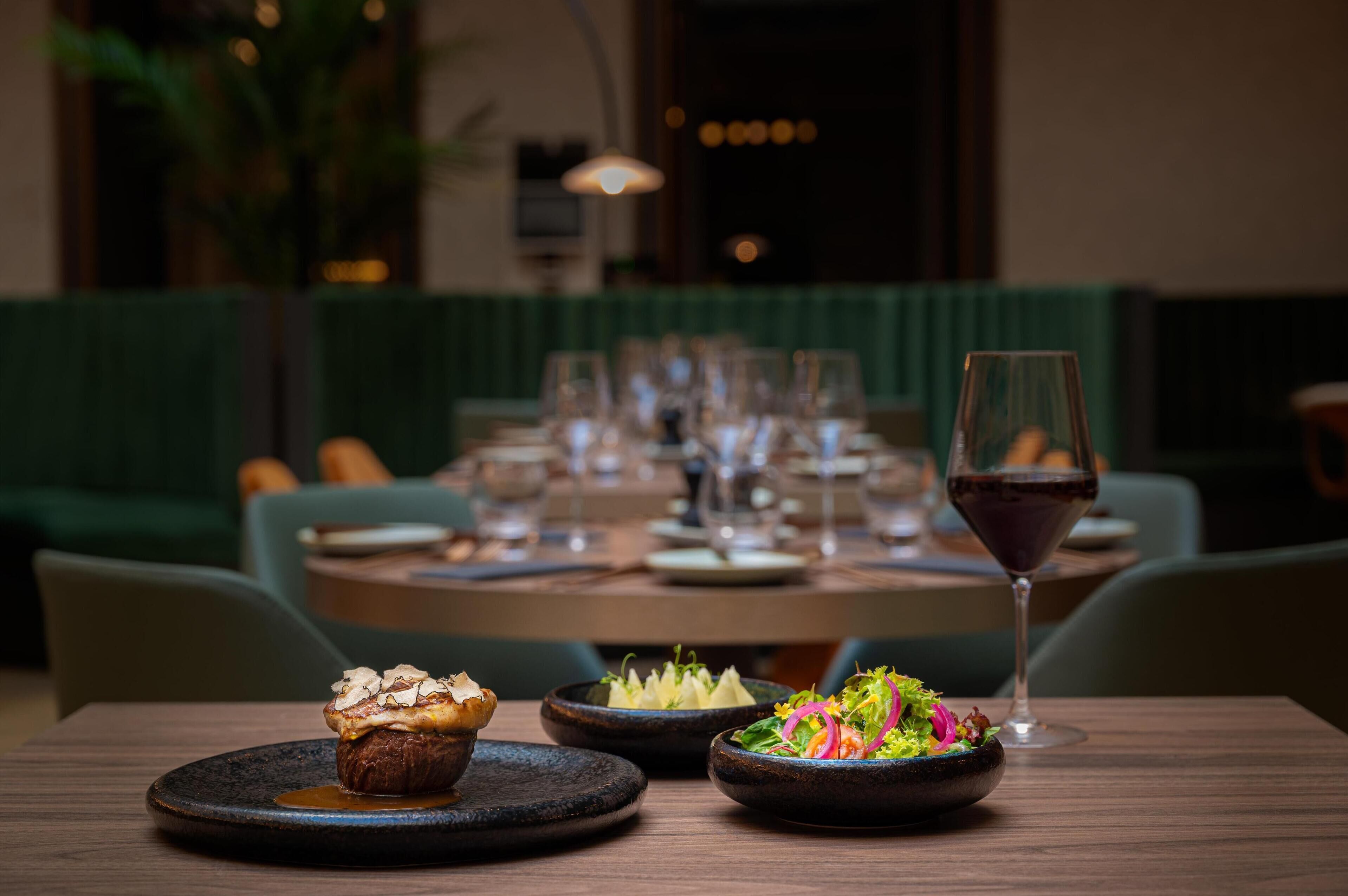 A dining table with plates of food, a glass of red wine, and a dessert.