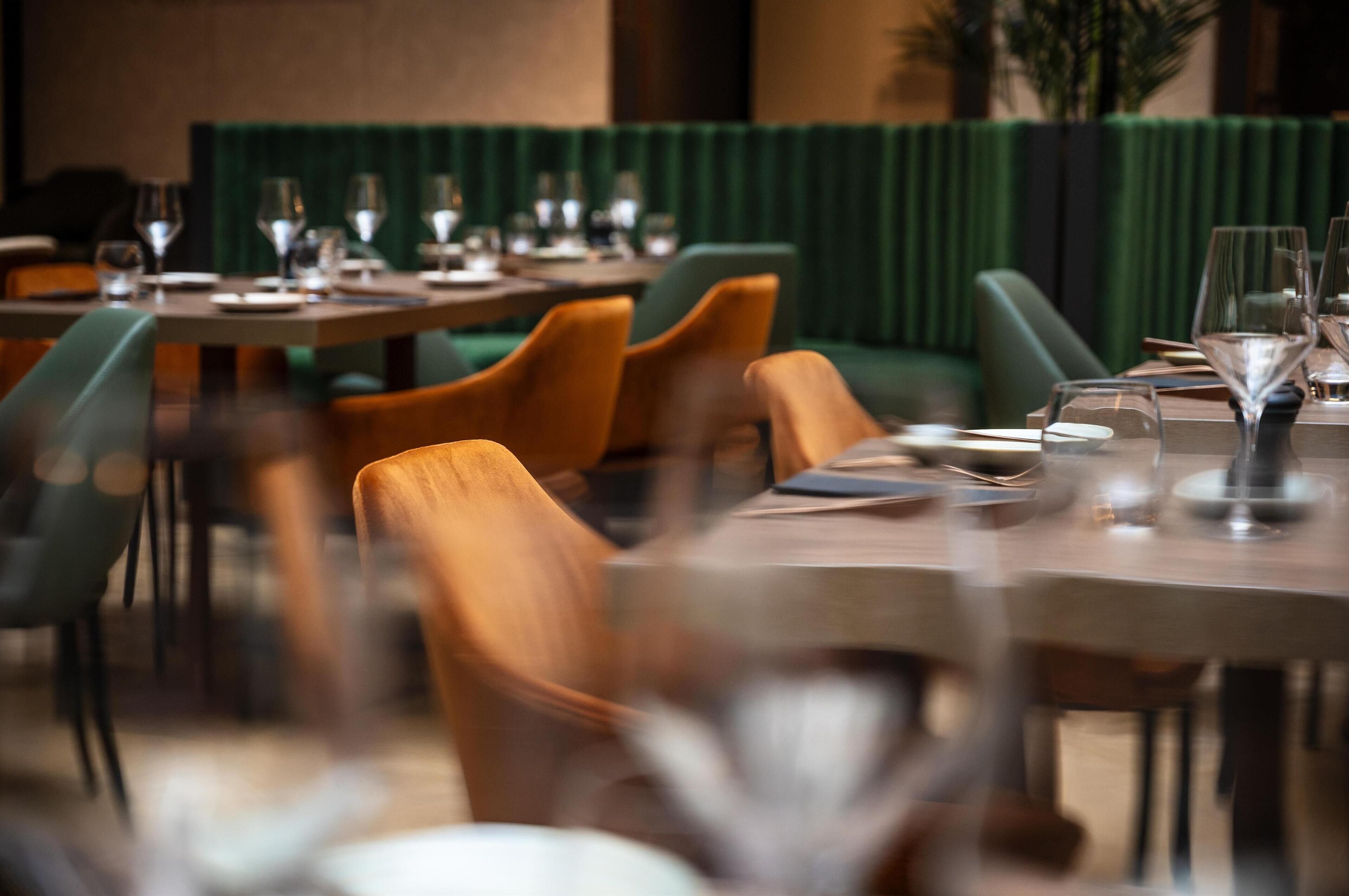 A restaurant with round tables, green upholstered chairs, and a green curtain backdrop.