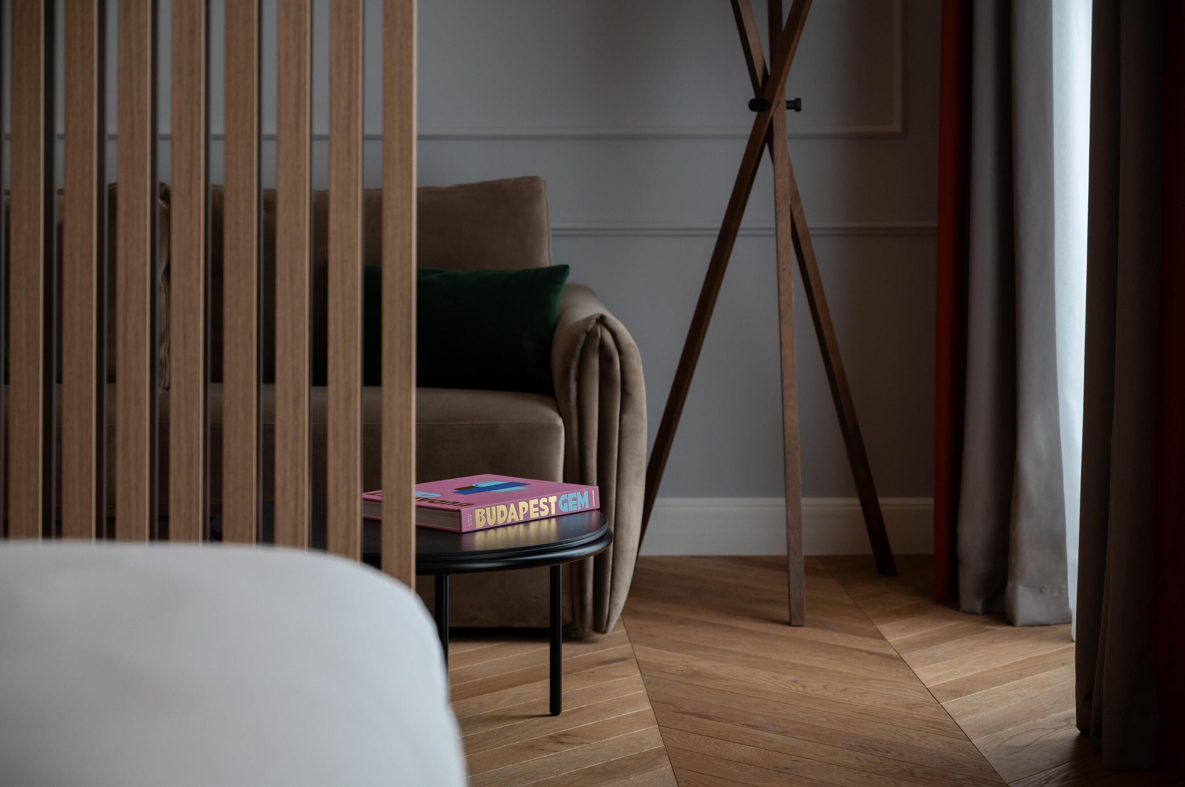 Una habitación con piso de madera, un sofá con un cojín verde y una mesa con un libro titulado 'BUDAPEST GEM'.
