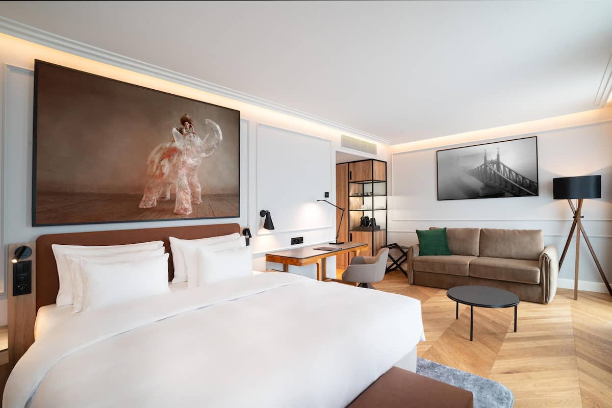A modern hotel room with a large bed, a desk, a sofa, and a coffee table.