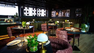 Un restaurante moderno con asientos cómodos, iluminación colgante y un amplio ventanal que exhibe sombreros.