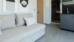 Een moderne woonkamer met een grijze bank, een houten deur en een keuken met grijze kastjes.
