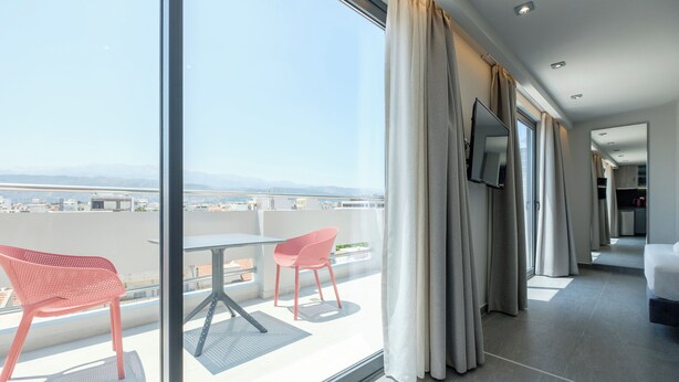 Een moderne hotelkamer met balkon, grote ramen en uitzicht op de stad.