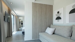 Een moderne hotelkamer met een grijze bank, een flatscreen televisie aan de wand en kunstwerken erboven.
