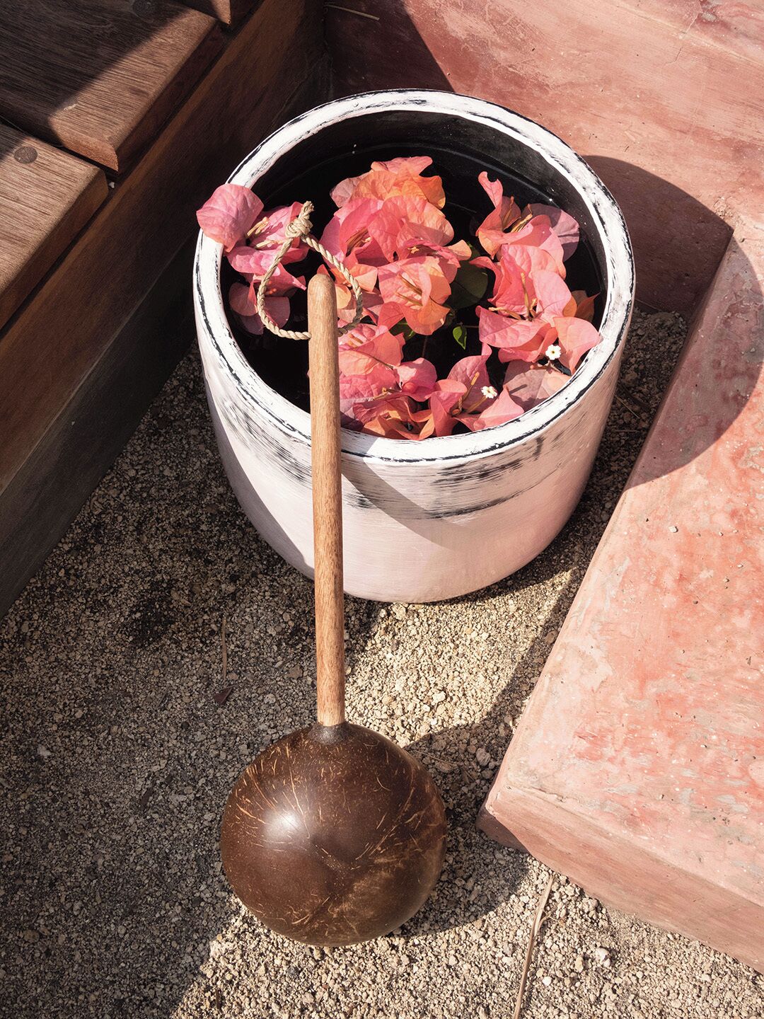 A wooden spoon in a white bucket filled with pink flowers.