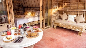 A rustic room with a bed, a sofa, and a dining table with breakfast items. - Villa Palma Gili Meno (Gili Meno)