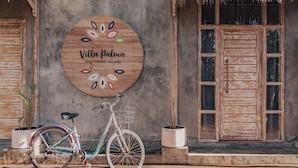 A bicycle parked in front of a building with a wooden sign that reads "Villa Palma Gili Meno Island." - Villa Palma Gili Meno (Gili Meno)