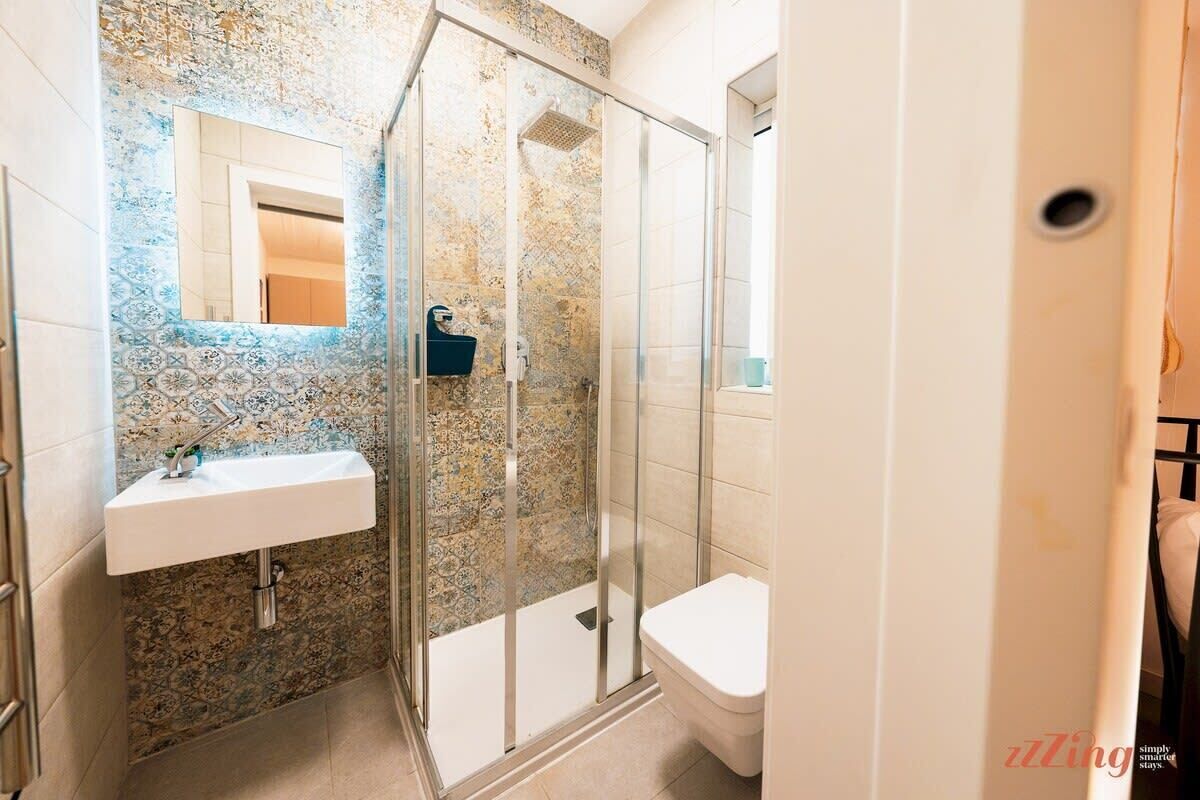 A bathroom with a glass shower enclosure, a white sink, and a toilet.