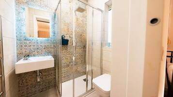 A bathroom with a glass shower enclosure, a white sink, and a toilet.