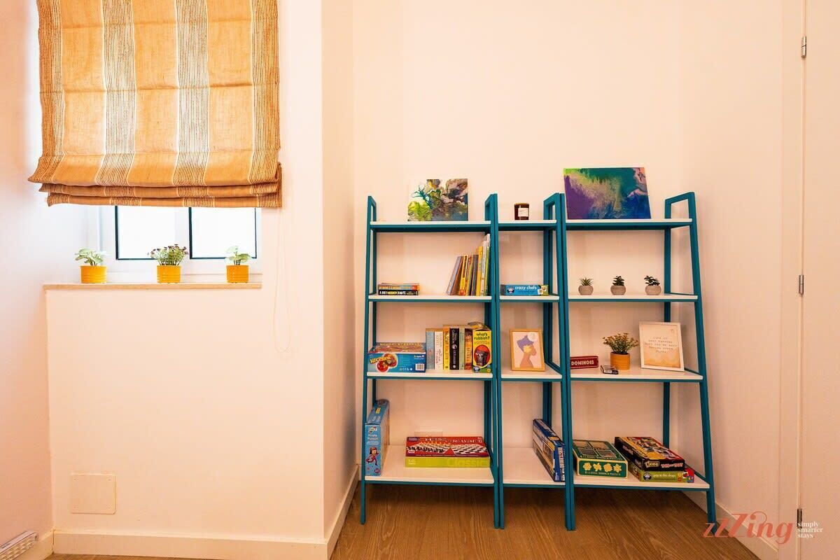 A room with a teal bookshelf filled with books and small decorative items, a window with blinds, and a radiator.