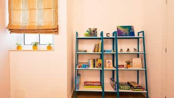 A room with a teal bookshelf filled with books and small decorative items, a window with blinds, and a radiator.