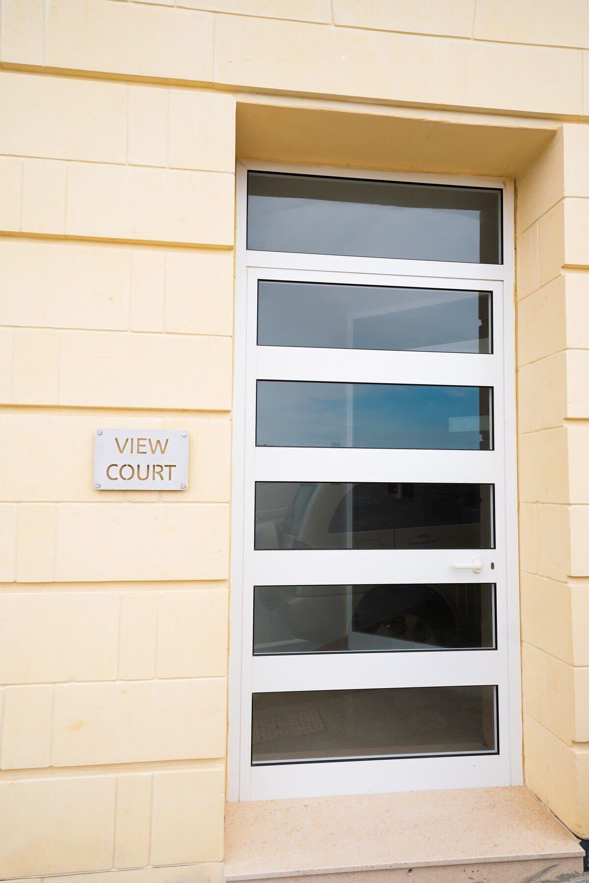 Une porte blanche avec de nombreux panneaux de verre et une pancarte indiquant « VUE SUR LE TERRAIN » sur le mur.