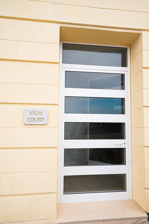 A white door with multiple glass panels and a 'VIEW COURT' sign on the wall. - Glamorous Apartment with Panoramic Green Views (Iz-Zebbug)