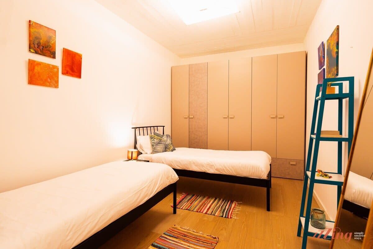 A bedroom with two single beds, a wardrobe, a ladder, and artwork on the wall.