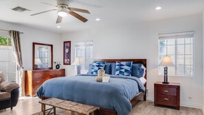 Une chambre à coucher comprenant un lit, des tables de chevet, un banc, un ventilateur de plafond et des fenêtres.