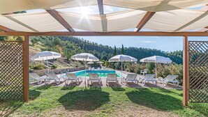 A pool area with lounge chairs and umbrellas, surrounded by a wooden pergola and a view of a hilly landscape. - Beautiful home in Dicomano with WiFi (Dicomano)